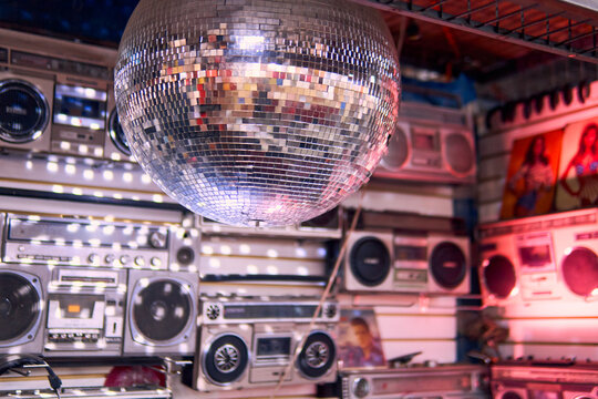 Audio product scene from the 70s and 80s. A silver disco ball lights up and a wall of vintage radios and retro boomboxes. Shiny and very colorful.