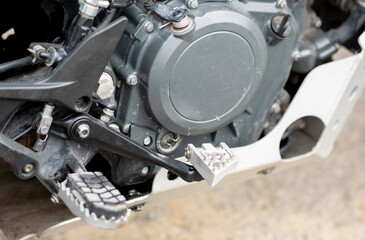 A daytime view of a black and orange recreational motorcycle with saddlebags. Its various components and mechanisms are visible. A view of the right engine cover, footrest, and rear brake lever.
