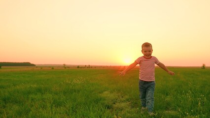 Happy kid boy laughs while playing on lawn. Little boy runs across green grass with arms raised. Happy family picnic, child in nature. Slow motion. Little child plays on lawn. Child's active games.
