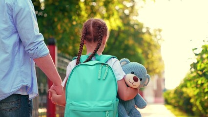Father little daughter schoolgirl, walk to school with backpack, child holding teddy bear. Parent father, child girl, walk together outdoors. Children's education concept. Happy family walk in park