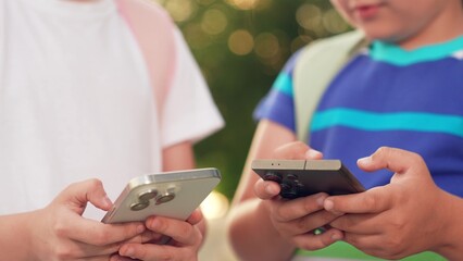 Kids boy girl play online games with phone in their hand on street. Modern technologies urban life. School children with backpack walk outdoors using smartphone. Children communicates using smartphone