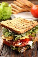 Tasty sandwich with bacon, cheese, vegetables and sauce on wooden table, closeup