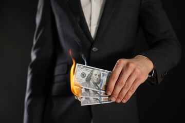 Man burning dollar banknotes on black background, closeup