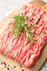 Raw minced meat with peppercorns and rosemary on table, closeup