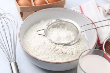 Ingredients for dough, whisk and strainer on white tiled table, closeup