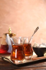 Tasty Turkish tea in glass cups, sweets and teapot on wooden table against brown background, closeup
