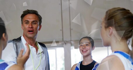 Addressing gymnasts, male sports instructor coaching near windows in gym, with whistle and leotards