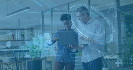 Pointing colleagues reviewing slim tablet in open-plan office, with floating digital HUD graphics