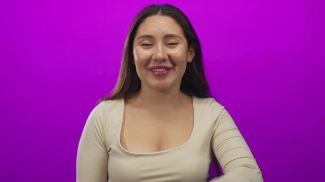 Woman with pink soft lips and raised hand blows kiss gesture in purple studio; affection longing desire.