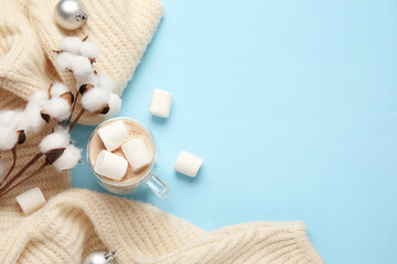 Naklejka na ściany i meble Cup of cocoa with marshmallows, cotton flowers and sweater on blue background. Hello winter Naklejka na ściany i meble Cup of cocoa with marshmallows, cotton flowers and sweater on blue background. Hello winter