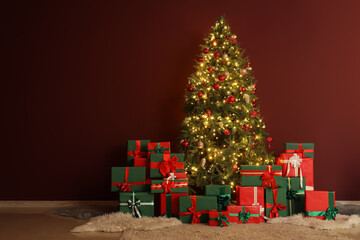 Glowing Christmas tree with presents near burgundy wall in room