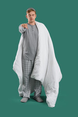 Male sleepwalker in pajamas with blanket on green background