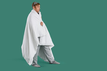 Male sleepwalker in pajamas with blanket on green background