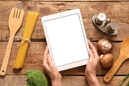 Female hands with digital recipe book, ingredients and kitchen utensils on wooden background - Powered by Adobe