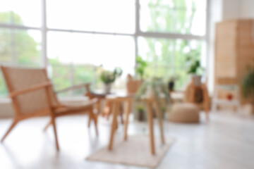 Blurred view of light room with wooden armchair, tables and green plants