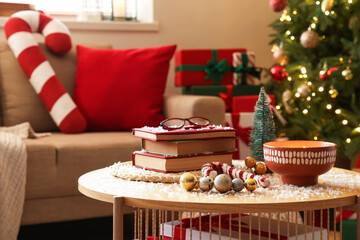 Books with eyeglasses, Christmas decor and snow on table in living room