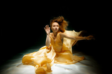 Fototapeta premium A Graceful Underwater Dance, Enveloped in Ethereal Yellow Fabric, Captivates the Eye