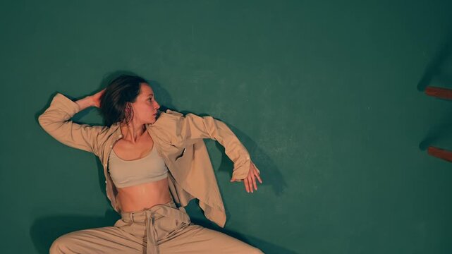 A professional young Caucasian ballerina stands against a studio wall embodying contemporary ballet. Through a blend of choreography and freestyle improvisation she expresses artistic creativity