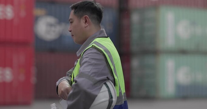 Logistics worker drinks water while taking a break at a shipping container yard. Emphasizing workplace hydration, occupational safety, and employee well-being in industrial environments.

