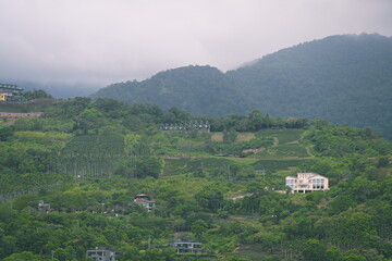 Fototapeta premium Layered green mountains with terraced rows and buildings, misty peaks in background viewed from Pobuwo area across Lanyang River, Sanxing, Yilan County, Taiwan.