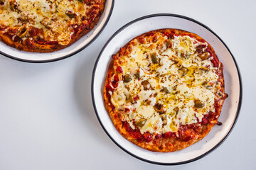 two small margherita pizzas with olives on bigger plates, portion control concept