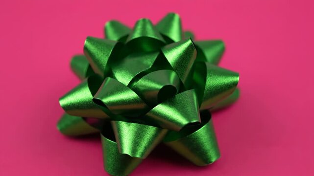 A single shiny green gift bow with a textured metallic finish is centered against a vibrant pink background, perfect for holiday or celebration themes vector illustration