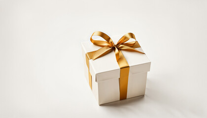 Fototapeta premium a square white gift box with a gold satin ribbon and bow, positioned centrally on a bright, smooth, blank white surface.