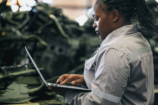 Female technician check used car damaged engine block at scrapyard warehouse recycle area part. African American engineer inspecting rust oily auto motor old spare part in junkyard for reuse service