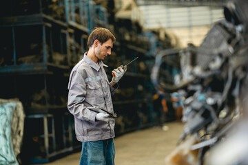 White man technician checking used car damaged engine block at scrap yard warehouse recycle area part. Maintenance engineer inspecting rust oily auto motor old spare part in junkyard for reuse service