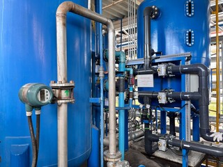 Industrial water treatment plant equipment, featuring blue tanks, pipes, and a flow meter, essential for purification and process control.