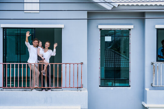 A happy family of three shares a loving moment on the balcony of their modern home. The daughter kisses her mother's cheek, showcasing joy, affection, and peaceful family life.