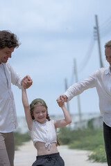 Fototapeta premium A happy young family holding hands while walking through a new residential neighborhood. The loving parents smile at their daughter, enjoying a peaceful stroll and quality time together.