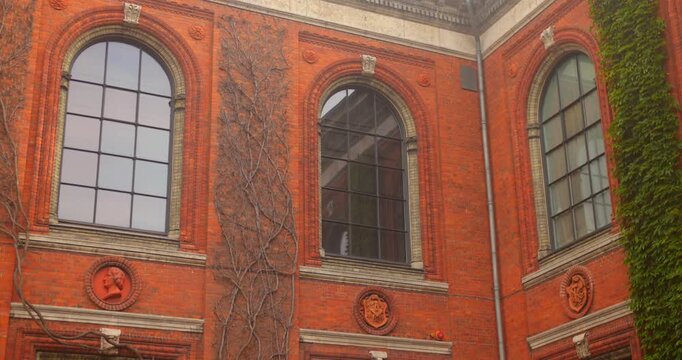 Historic red brick facade of Charlottenborg Palace in Copenhagen, Denmark. Features Baroque architecture, large arched windows, and climbing bare ivy. Home to the Royal Danish Academy of Art