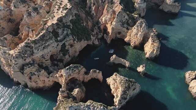Aerial drone performs a helix orbit, circling above the limestone arches, sea stacks, and small boats nestled in the turquoise waters of Ponta da Piedade near Lagos, Portugal.