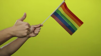 Man holding rainbow flag with thumbs up against vibrant yellow wall symbolizing lgbtq pride and support, emphasizing positivity and inclusivity.