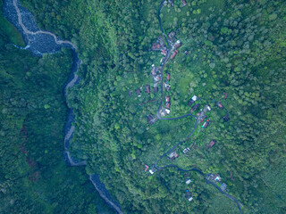 Aerial view Kabut Pelangi Waterfall in East Java. The waterfall stream flows into the mountain gorge in a long path.Above is the residence of the villagers. Abundance of forests on the green mountain