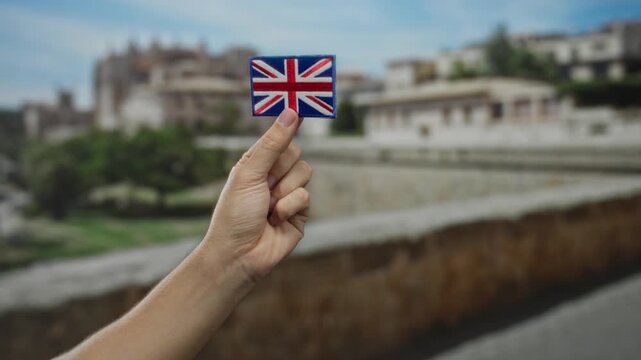 Caucasian man holding a british flag patch with embroidered details in an outdoor city setting, showcasing a blend of culture and urban environment.