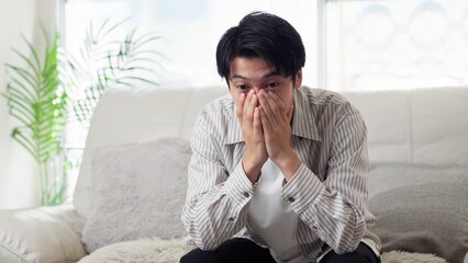 ソファで落ち込むアジア人男性