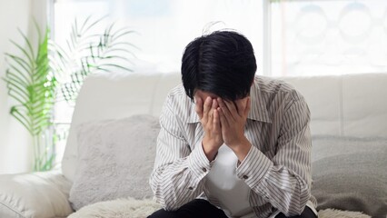 ソファで落ち込むアジア人男性