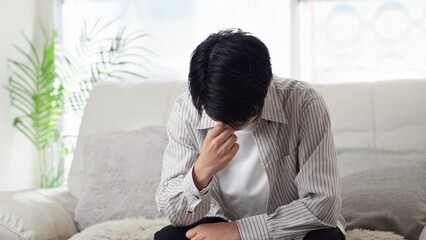 ソファで落ち込むアジア人男性