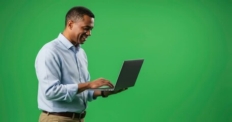 Smiling man using laptop against green screen backdrop in studio. - Powered by Adobe