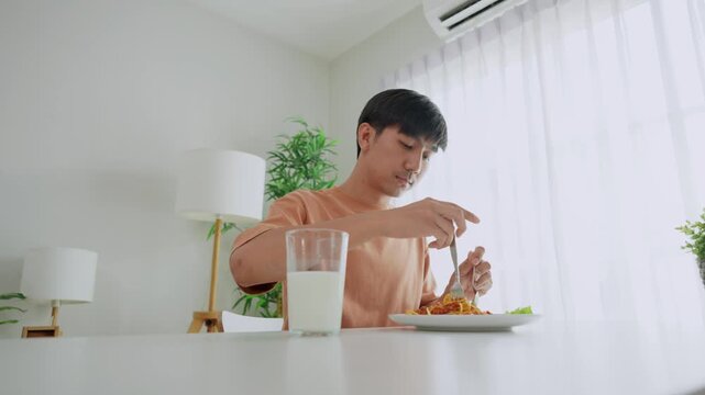 Asian handsome young man eating spaghetti and dimsum in kitchen at home.