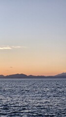 Serene ocean view at sunset with distant mountains creating a tranquil, peaceful scene perfect for travel or relaxation themed projects and creative content