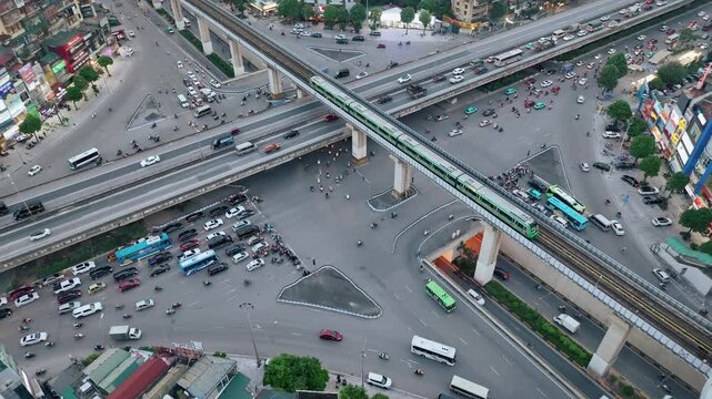 Aerial drone shot of Hanoi intersection with elevated metro line, buses, and cars at dusk.