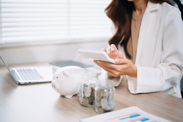 Asian woman saving for retirement Saving money through a piggy bank and taking notes in modern...