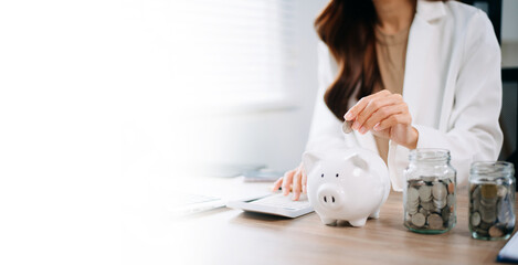 Asian woman saving for retirement Saving money through a piggy bank and taking notes in modern...