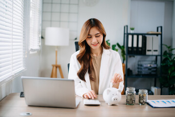 Asian woman saving for retirement Saving money through a piggy bank and taking notes in modern...