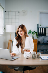 Asian woman saving for retirement Saving money through a piggy bank and taking notes in modern...