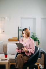 Young Asian woman sitting on the sofa with laptop celebrating success in cozy living room