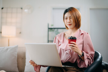 Young woman sits comfortably on a sofa, reading a notebook while holding a coffee cup.
